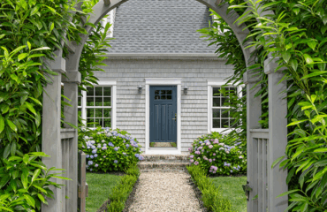 Main Exterior Entrance Exterior front view of a home featuring a dark navy blue front entry door with glass panels, surrounded by double-hung windows, an arched wooden trellis, stone pathway, and lush garden landscaping.