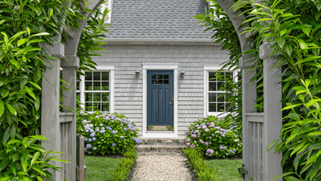 Main Exterior Entrance Exterior front view of a home featuring a dark navy blue front entry door with glass panels, surrounded by double-hung windows, an arched wooden trellis, stone pathway, and lush garden landscaping.