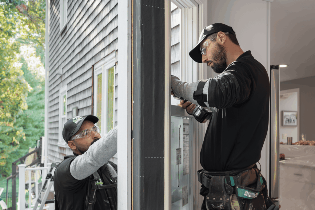 A professional technician installing a new replacement window on a home exterior.