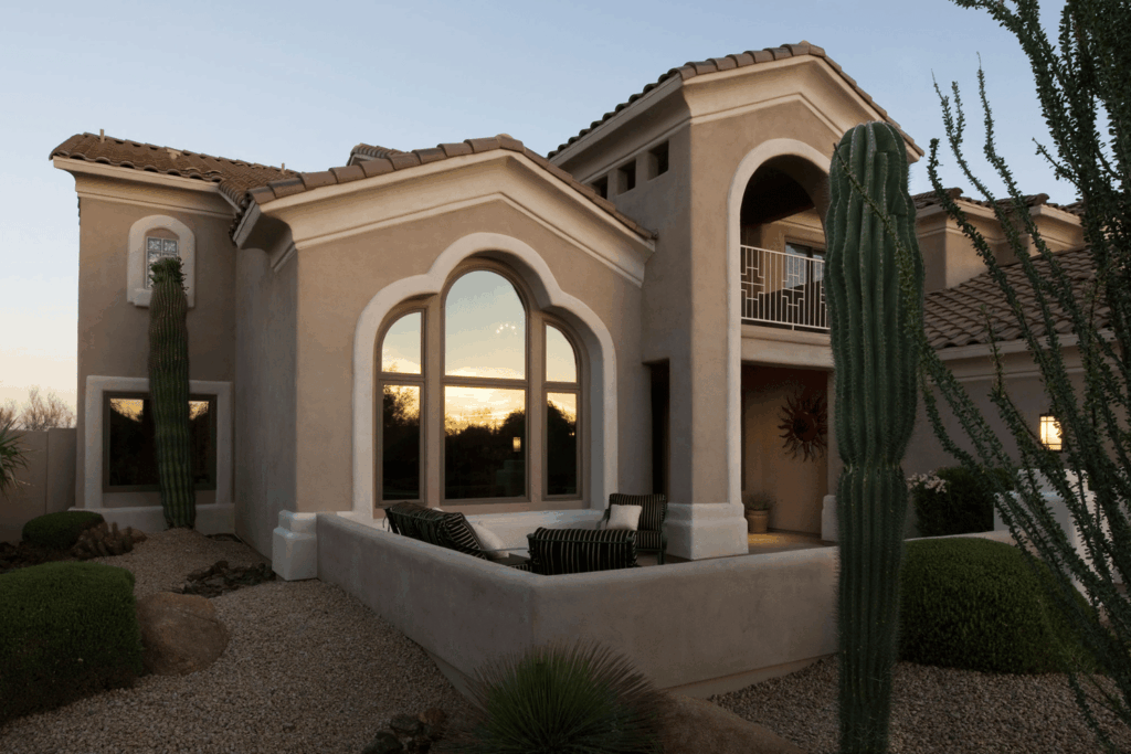 Exterior front view of a two-story beige stucco house with dark-framed replacement windows, an arched front door, and a multi-car driveway.