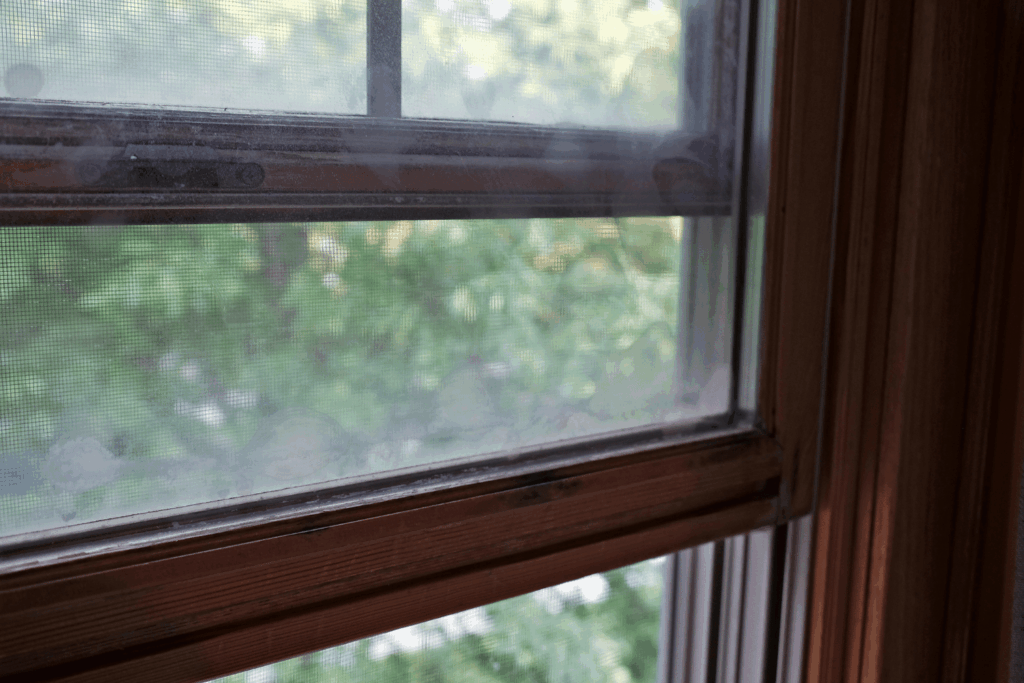 Close-up view of a dark wooden window frame with a hand operating the sliding lock mechanism.